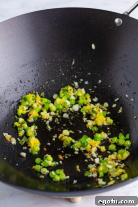 A wok with green onion, garlic, ginger, and chili flakes.