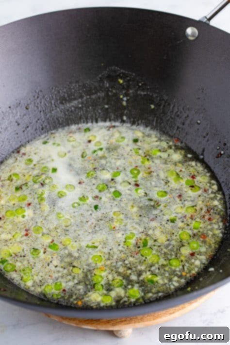 A wok with green onion, garlic, ginger, lemon juice, water, sugar, salt and pepper.