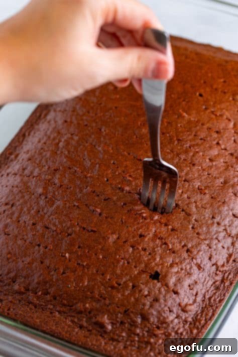 Heavenly Oreo Dream Cake 13 A fork poking holes in a devil's food chocolate cake.