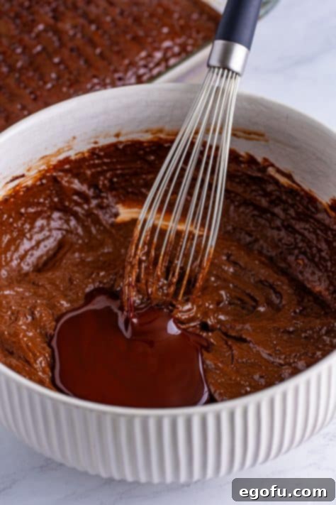 Heavenly Oreo Dream Cake 15 Chocolate syrup being mixed into pudding and milk in a mixing bowl.