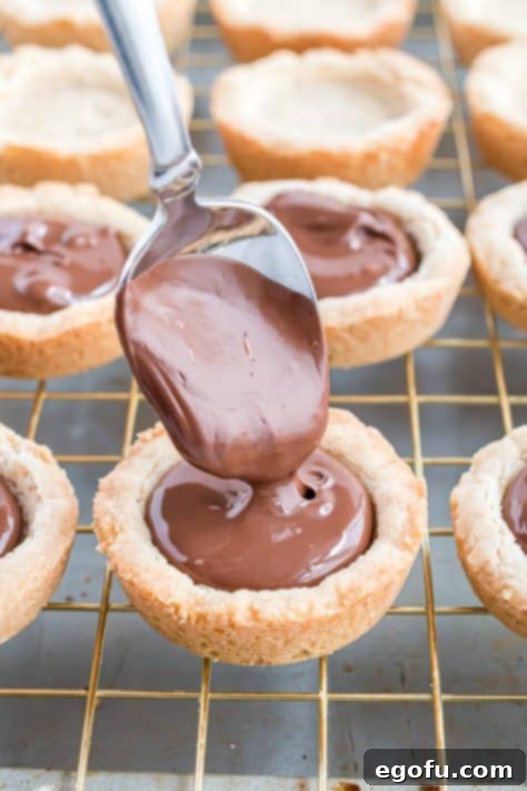 a spoon pouring melted chocolate into cookie cups.
