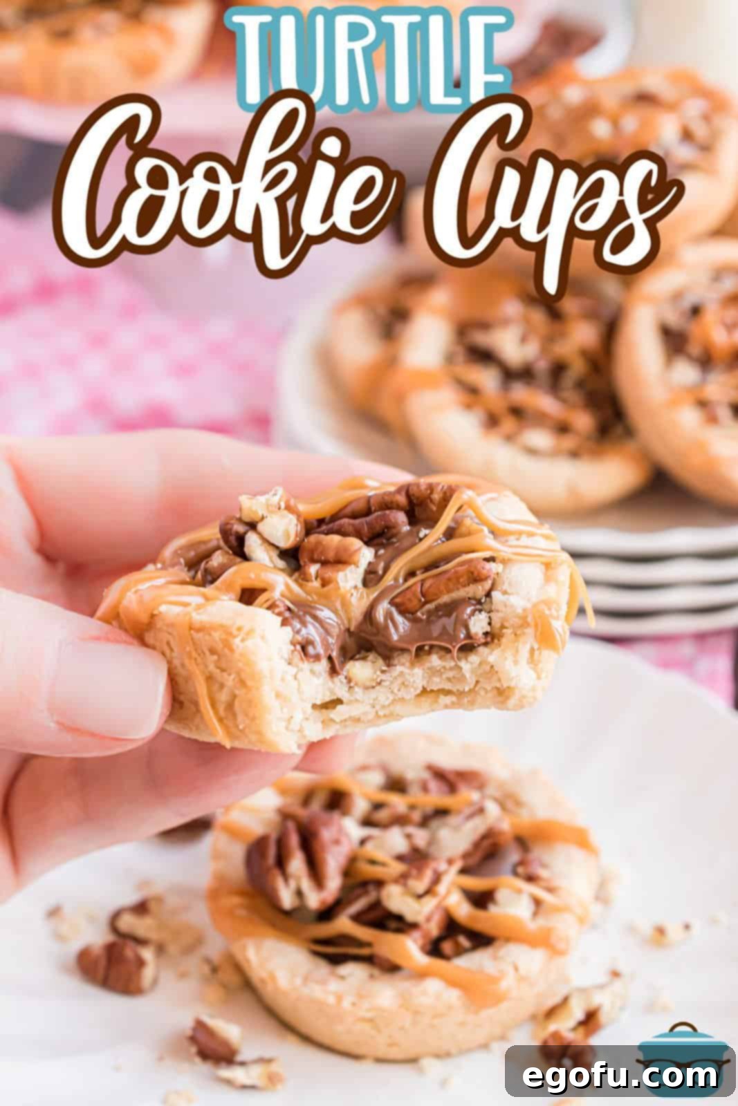A hand holding a Turtle Cookie Cup with a bite taken out, revealing the soft cookie, melted chocolate, and gooey caramel with pecans.