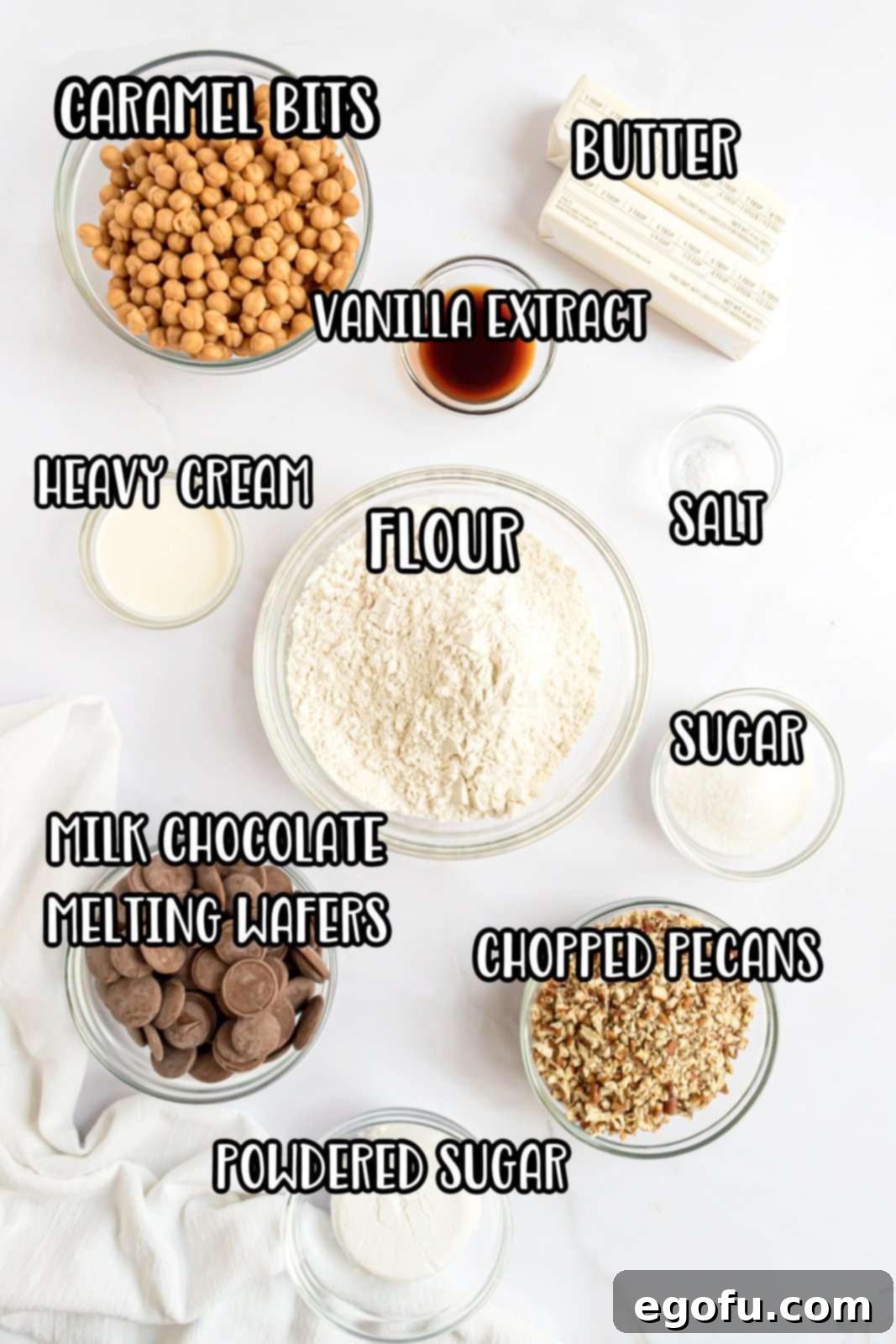 A vibrant flat lay of all the ingredients needed for Turtle Cookie Cups, including unsalted butter, granulated sugar, powdered sugar, vanilla extract, flour, salt, milk chocolate chips, caramel bits, heavy cream, and chopped pecans.