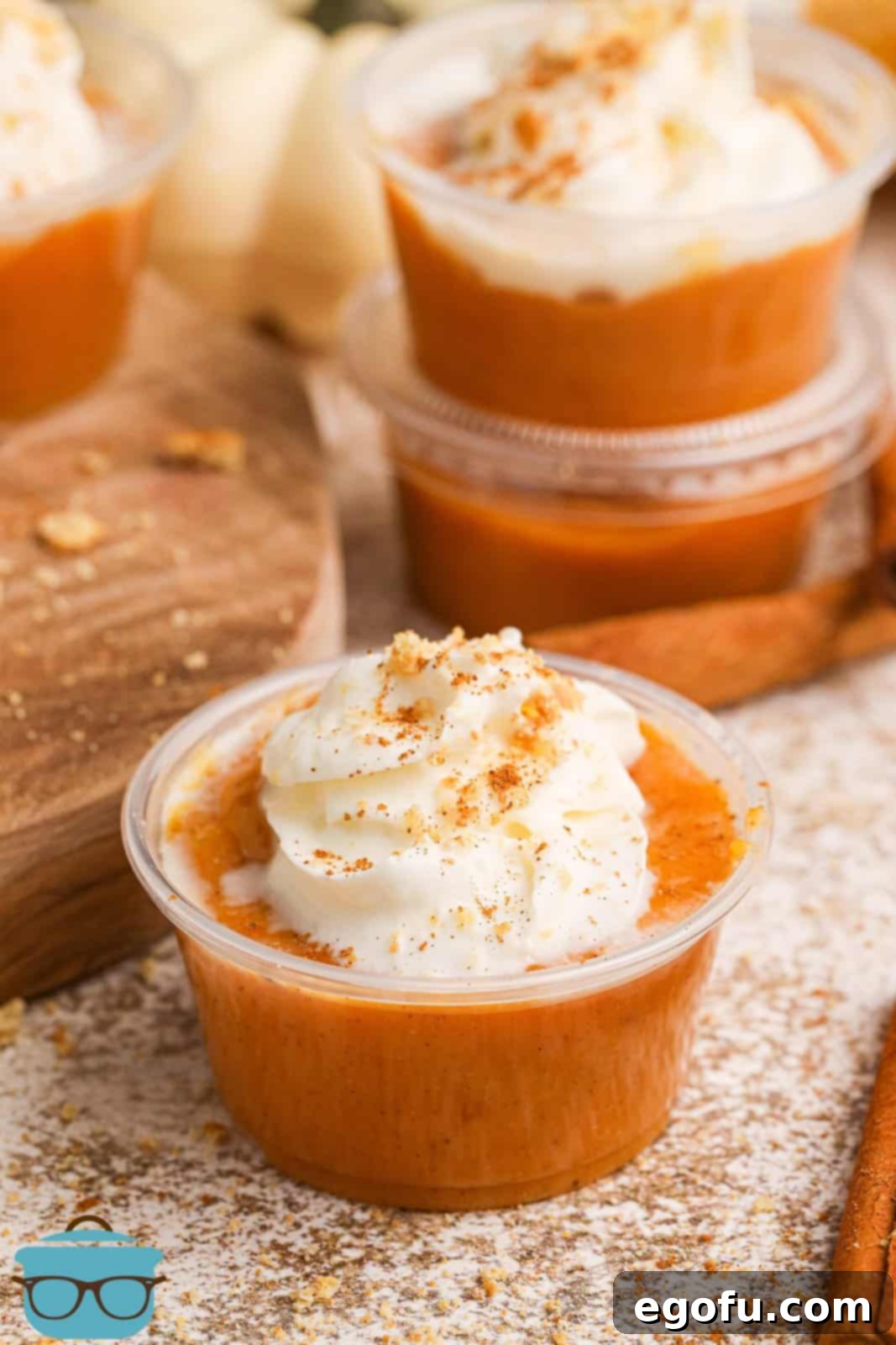 A close-up view of several beautifully garnished pumpkin pie shots, topped with fluffy whipped cream and a sprinkle of ground cinnamon, ready to be enjoyed.