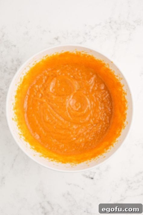 Vanilla pudding with milk, vodka, whiskey, pumpkin puree and pumpkin pie spice in a large mixing bowl.