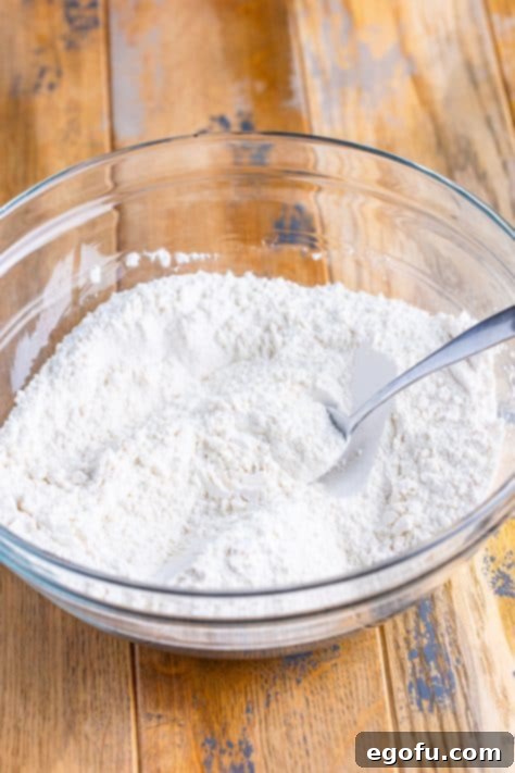 A glass mixing bowl of flour, sugar and baking powder.