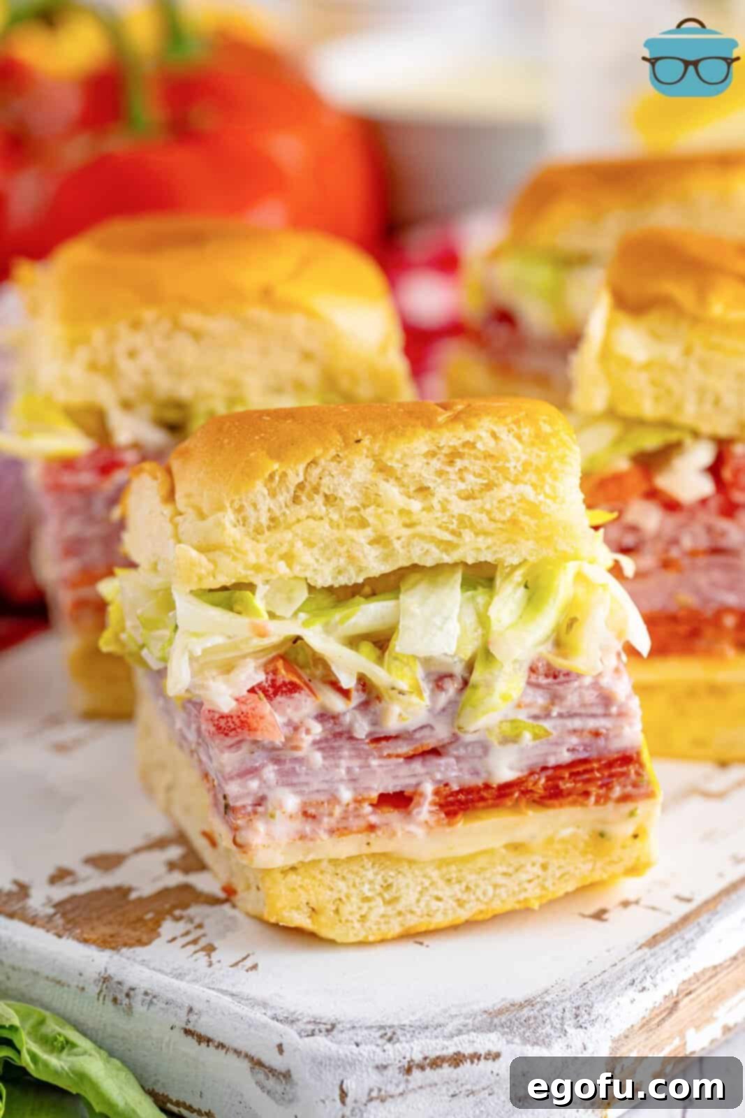 A few Italian Grinder Sliders on a small serving platter, showcasing layers of meat, cheese, and vegetables with a golden-brown bun.