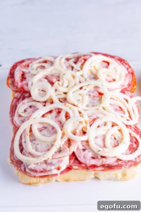 Tomatoes and onions layered on top of deli meat and cheese on slider buns.