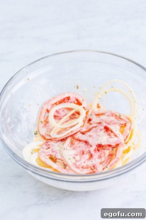Sliced tomatoes and onions with dressing in a mixing bowl, lightly coated.