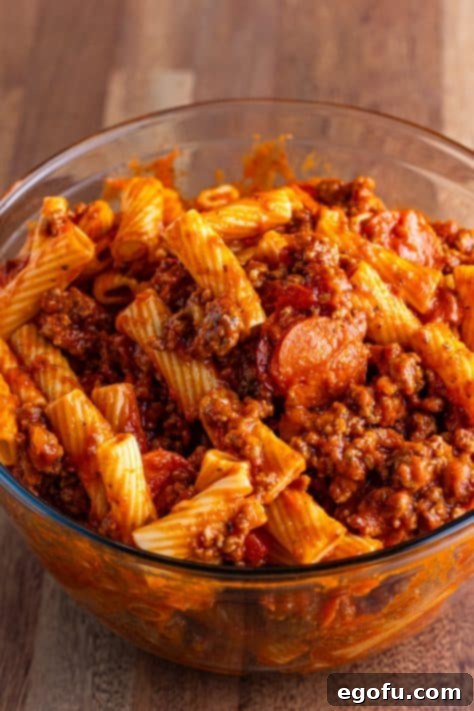One-Pot Pizza Magic 9 Cooked rigatoni, pizza sauce, pepperoni, sausage, ground beef, and onion mixed in a bowl.