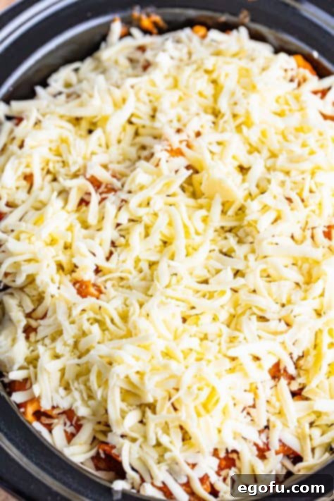 One-Pot Pizza Magic 13 The remaining cheese on top of the pasta mixture in a slow cooker, ready for cooking.