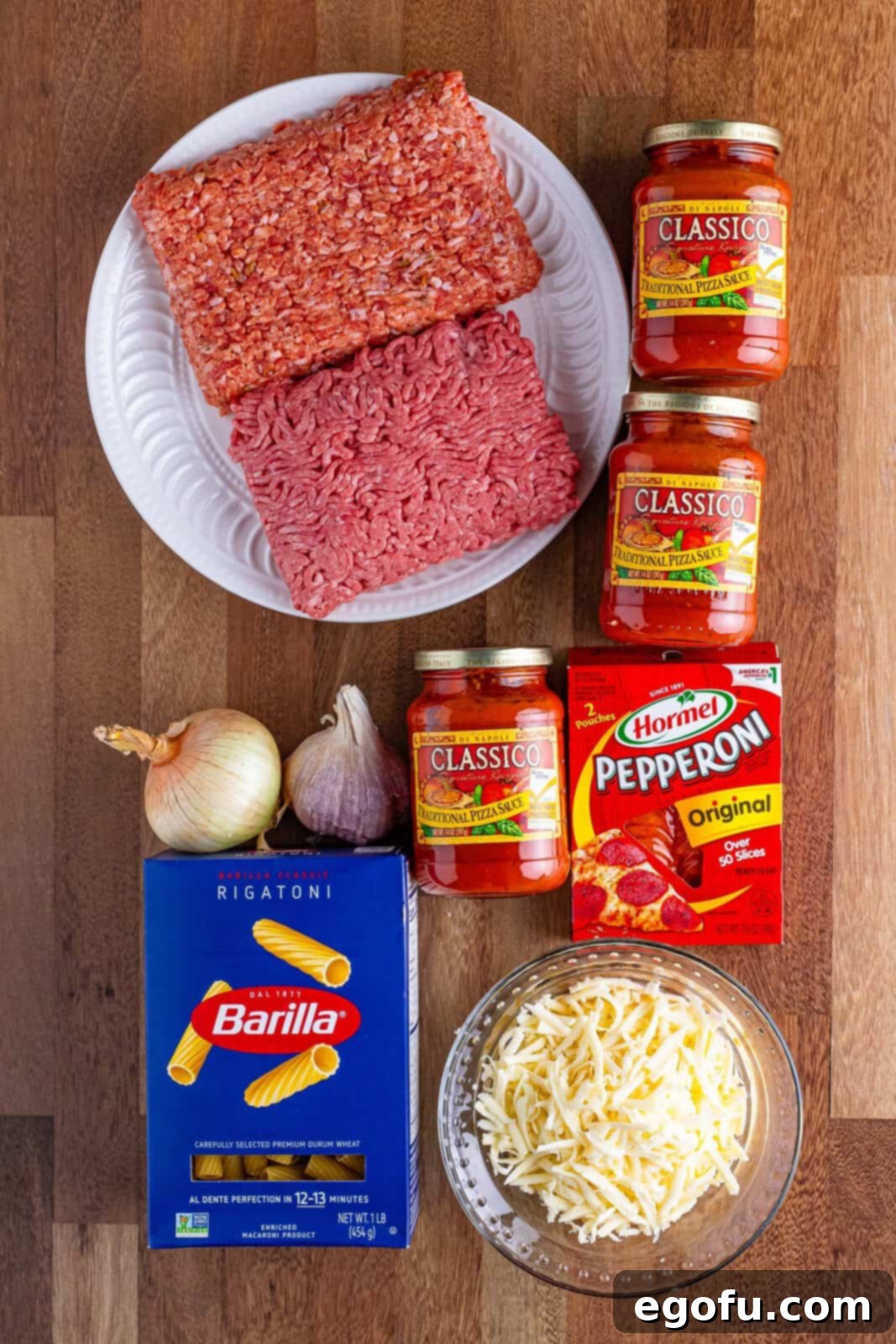 One-Pot Pizza Magic 4 A flat lay of Crock Pot Pizza Casserole ingredients including ground beef, sausage, pizza sauce, pepperoni, onion, shredded cheese, garlic, and rigatoni.