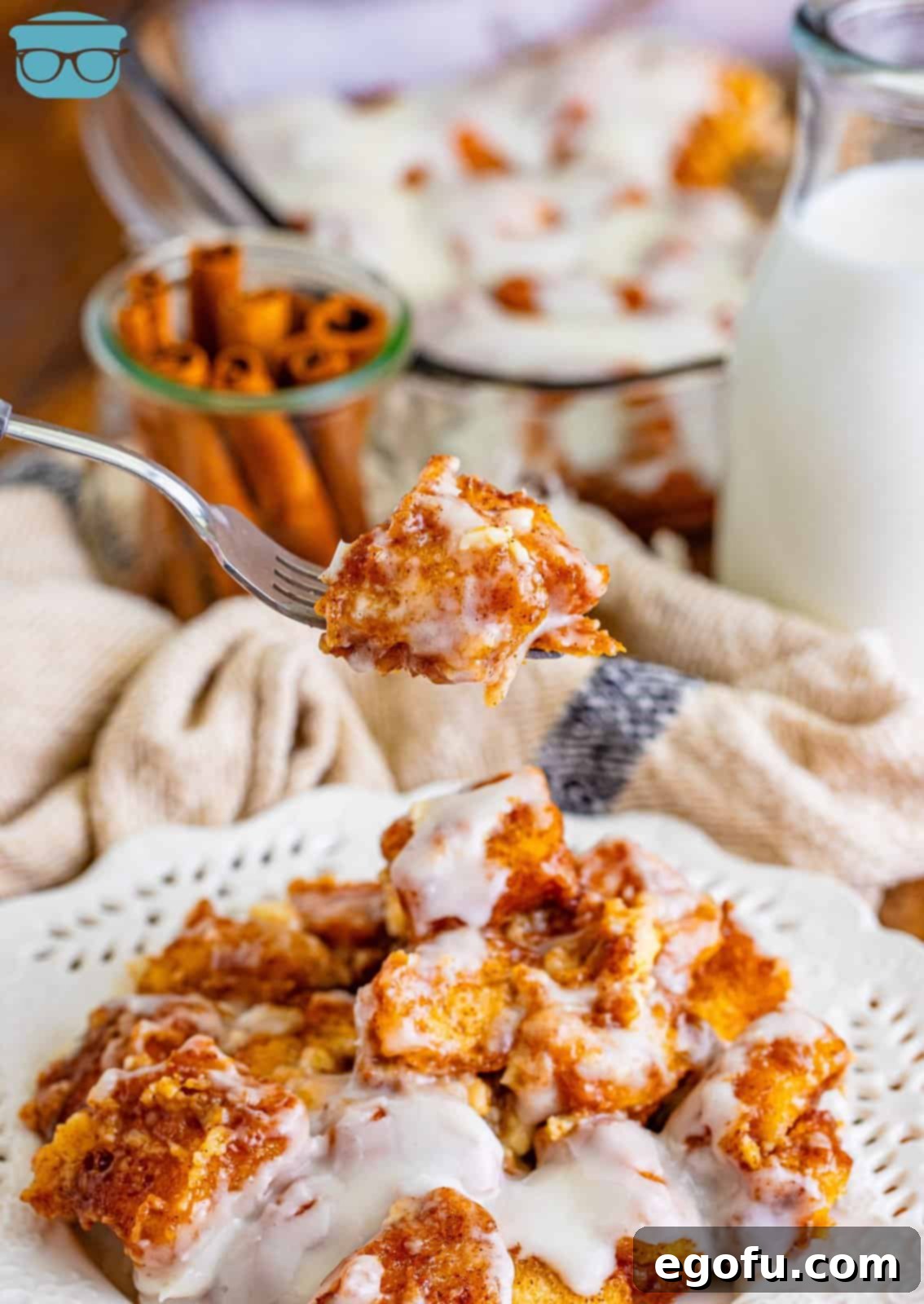 A fork lifting a delicious bite of Cinnamon Roll Bubble Up, showing the fluffy biscuit texture and melted glaze, held above a full plate of the casserole.