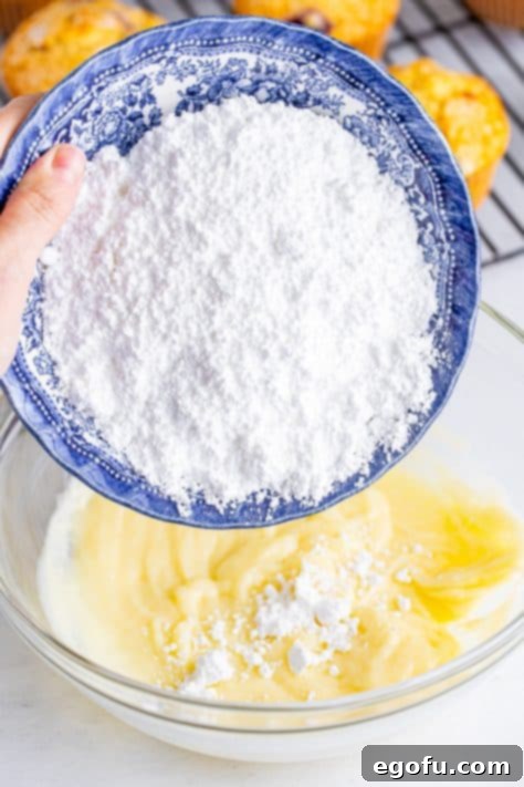 Powdered sugar being added to white chocolate and cream cheese.