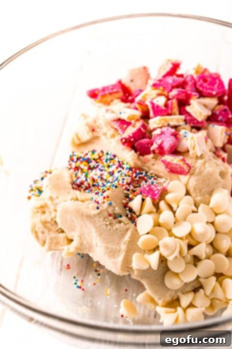 A mixing bowl with sugar cookie dough, white chocolate chips, circus animal cookie crumbs, and rainbow sprinkles.