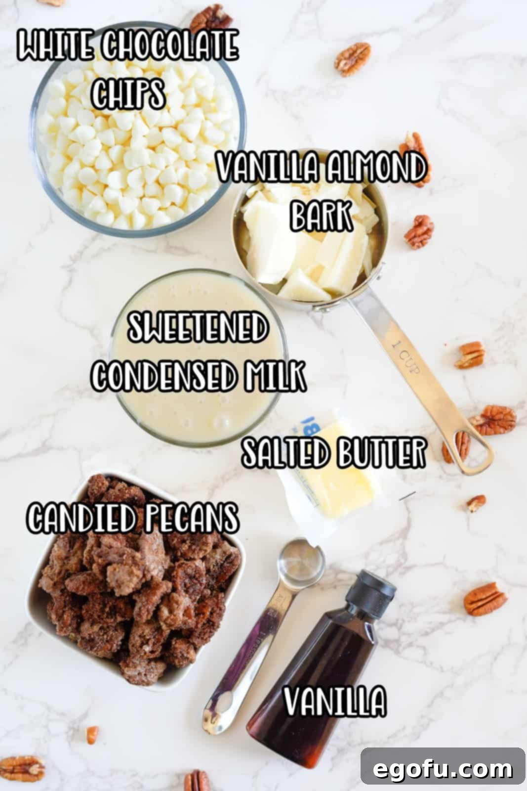 An assortment of ingredients laid out: butter, white chocolate chips, sweetened condensed milk, vanilla extract, candied pecans, and vanilla almond bark.