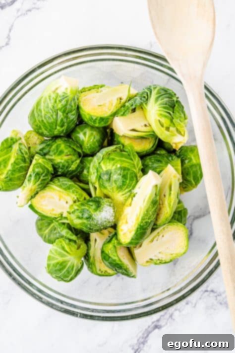 Crispy Holiday Brussels Sprouts 11 A glass mixing bowl with brussels sprouts, oil and salt.