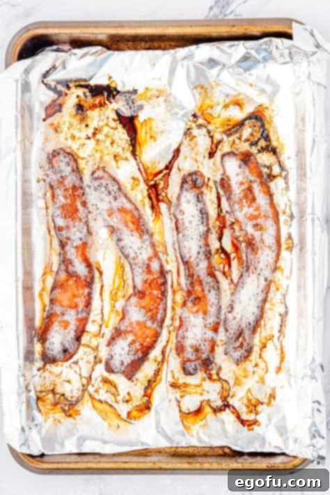 Crispy Holiday Brussels Sprouts 14 Cooked bacon on an aluminum foil lined baking sheet, draining.