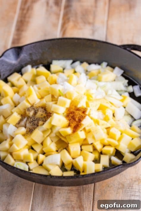 A skillet with bacon grease, potatoes, onion, pepper, creole seasoning, and salt.
