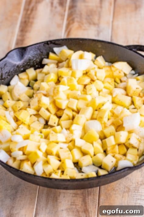 A skillet with bacon grease, potatoes, onion, pepper, creole seasoning, and salt all tossed together.