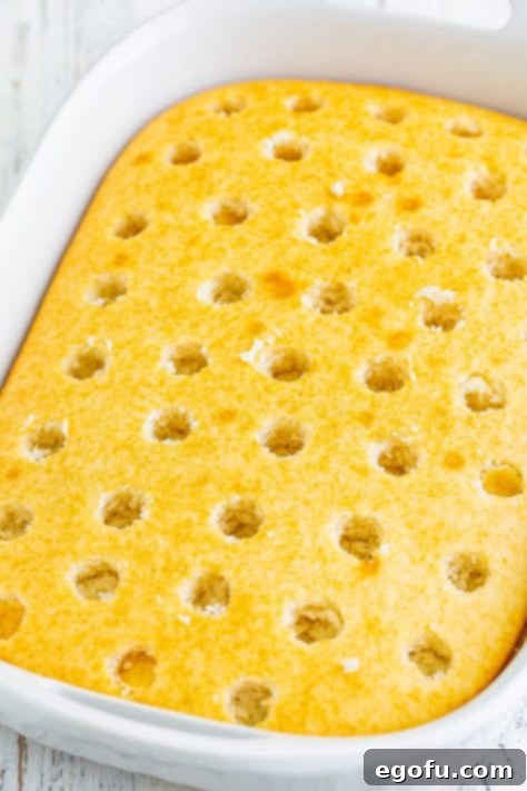 A freshly baked cake with numerous evenly spaced holes poked into its surface, ready for gelatin.