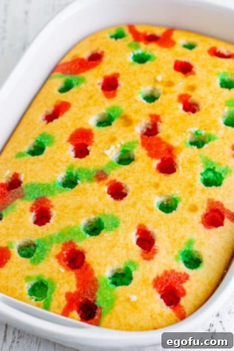 A baked cake with holes skillfully filled with alternating red and green Jell-O, demonstrating the 'poke' technique.