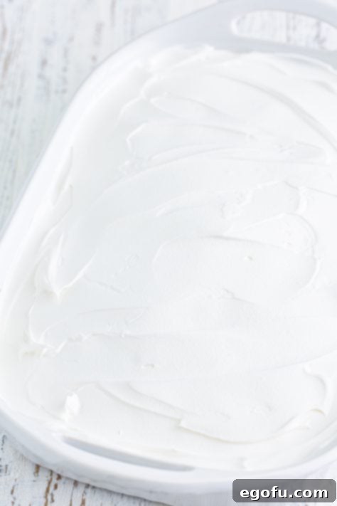 A baked cake generously covered with a smooth, fluffy layer of whipped topping, ready for final decoration.