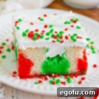 A vibrant slice of Christmas Jell-O Poke Cake with red, white, and green layers, ready to be served.