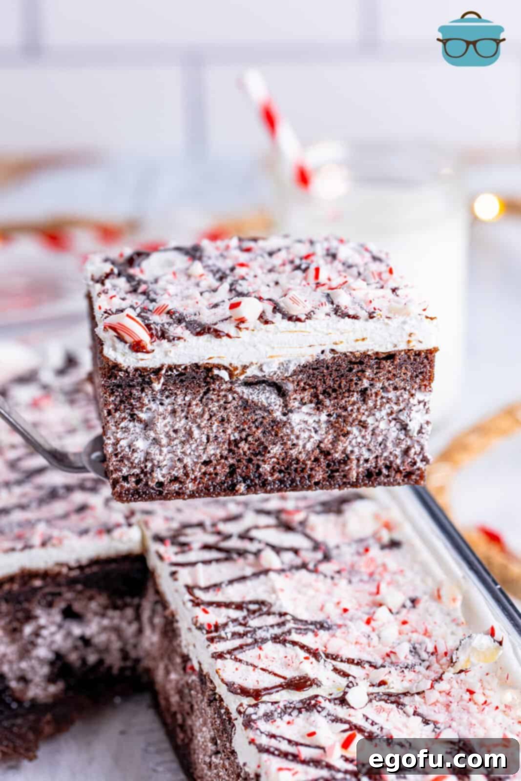 A slice of Peppermint Poke Cake being lifted from the baking dish by a serving utensil, showcasing its layers.