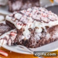 A plate with a slice of Peppermint Poke Cake with a fork holding a bite.