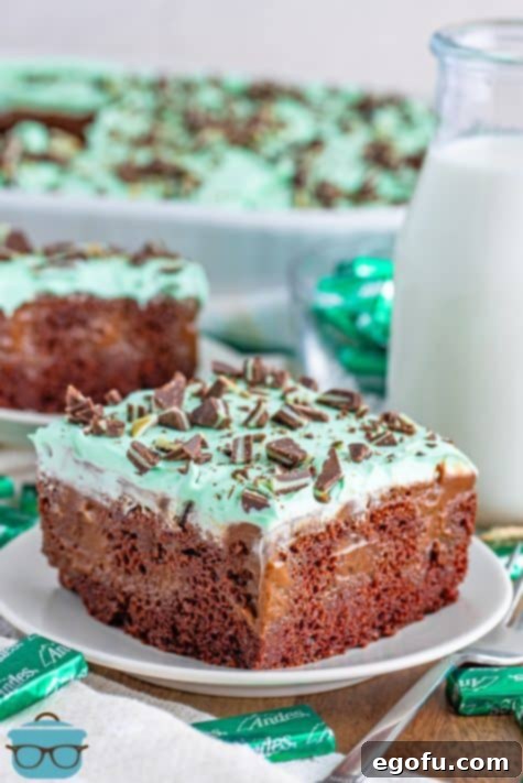Peppermint Patty Poke Cake 16 A piece of homemade Mint Chocolate Poke Cake on a white serving plate in front of the rest of the cake in a baking dish.