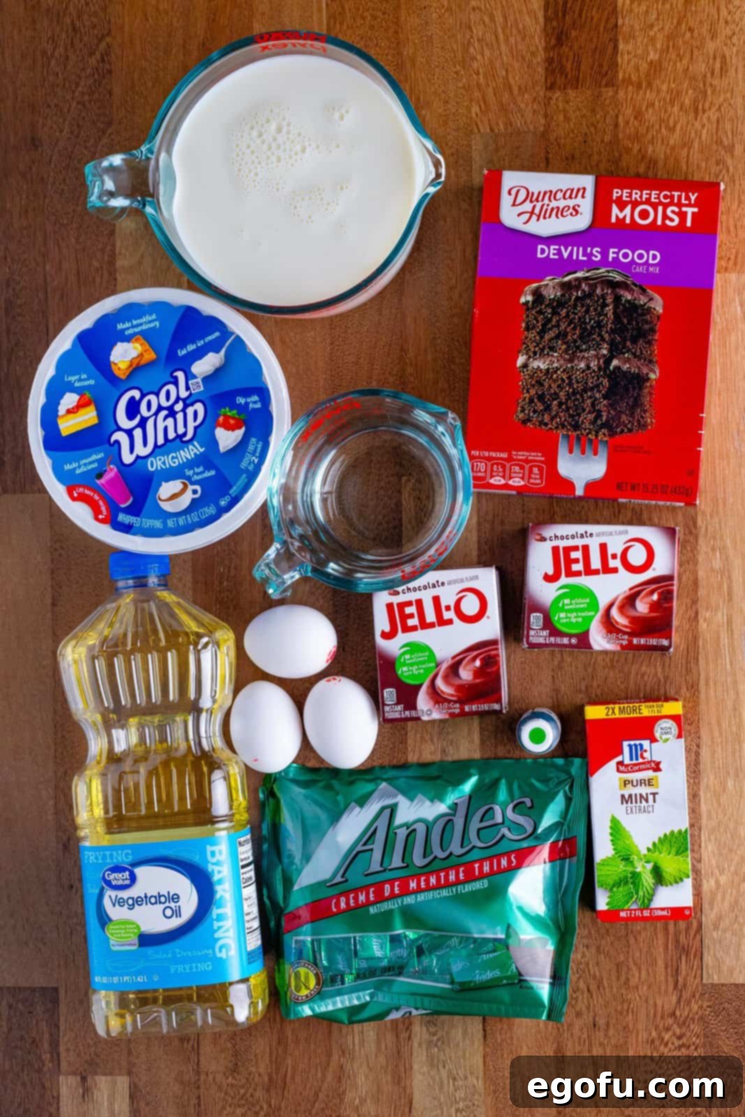 Peppermint Patty Poke Cake 3 A flat lay photograph showcasing all the ingredients required for Mint Chocolate Poke Cake: Devil's food cake mix, whipped topping, oil, water, eggs, chocolate pudding mix, Andes mints, mint extract, and milk.