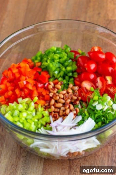 Zesty Black Eyed Pea Salad 5 A glass bowl of black-eyed peas, tomatoes, red bell pepper, green bell pepper, celery, green onions, and shallots.