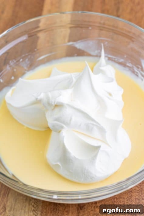 Whipped topping being added to a mixing bowl with cream cheese mixture.