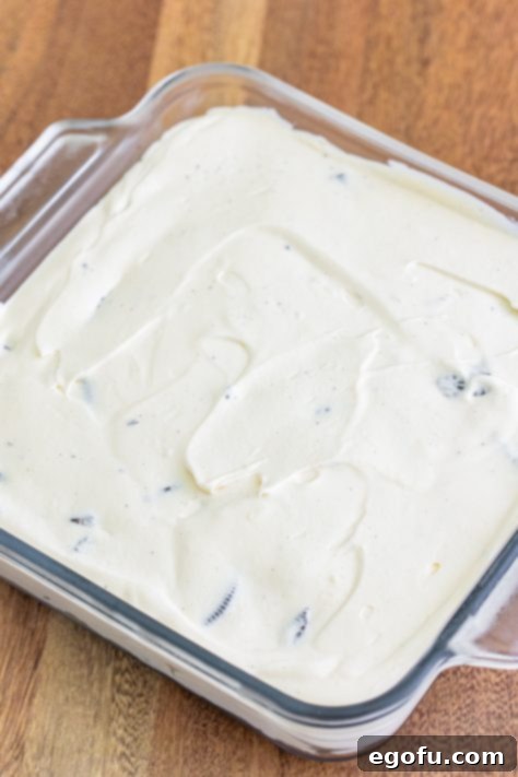 The cream cheese Oreo mixture is spread out over top of Oreo cookie crumbs in a baking dish.