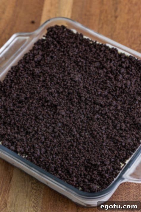 Cookie crumbs on top of cream cheese mixture on a bed of more cookie crumbs in a baking dish.