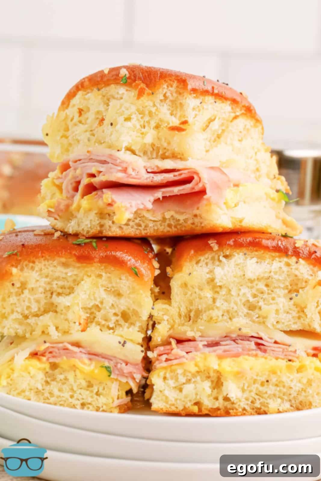 Three golden brown Honey Mustard Ham Sliders stacked on a plate, showing melted cheese and the buttery glaze.