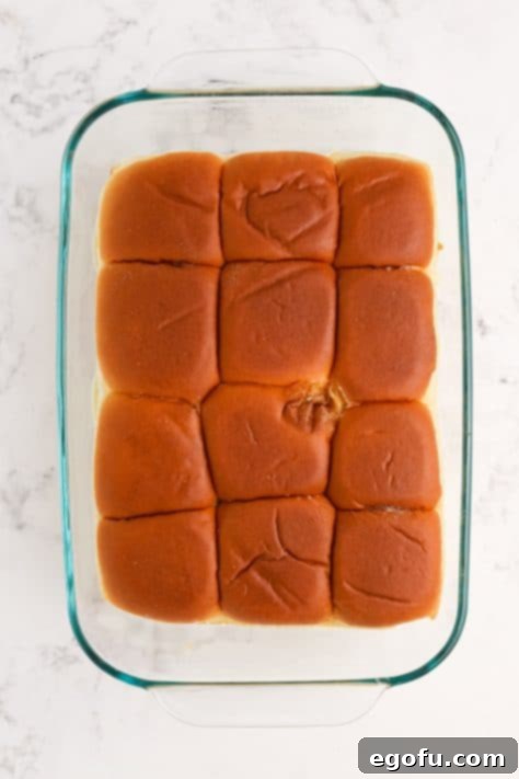Slider rolls on top of sandwiches in a baking dish.