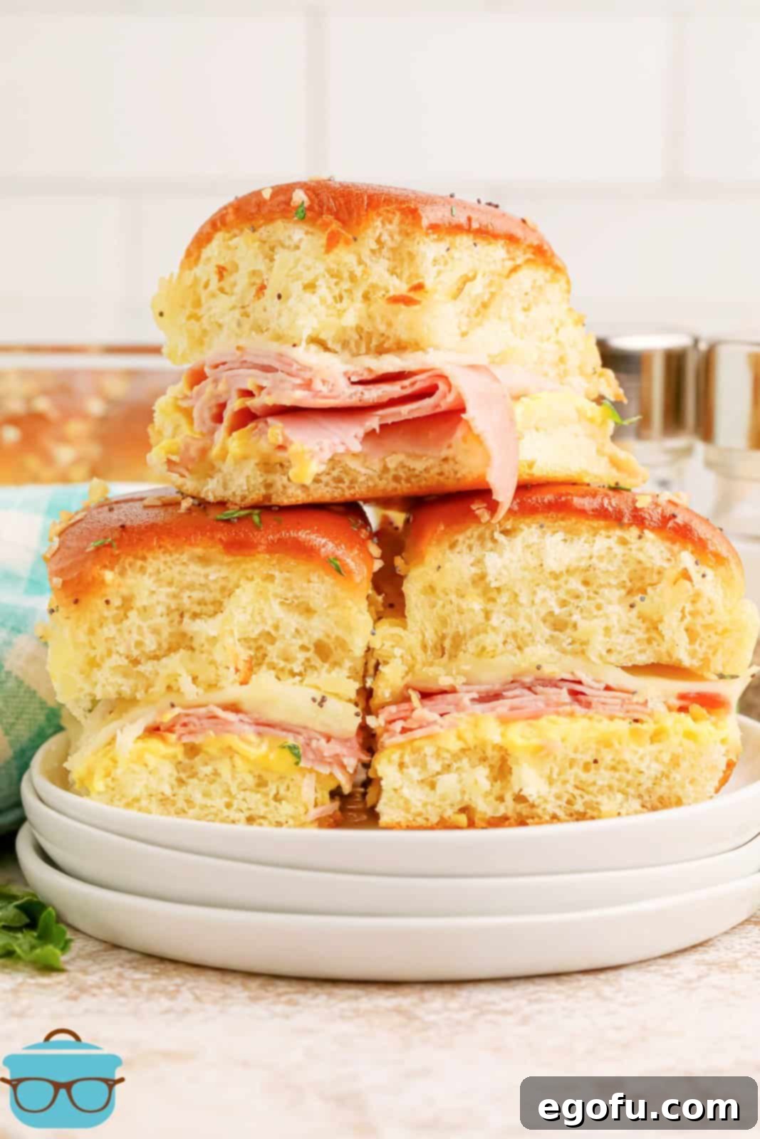 A small pyramid stack of freshly baked Honey Mustard Ham Sliders on a serving plate, garnished with parsley.