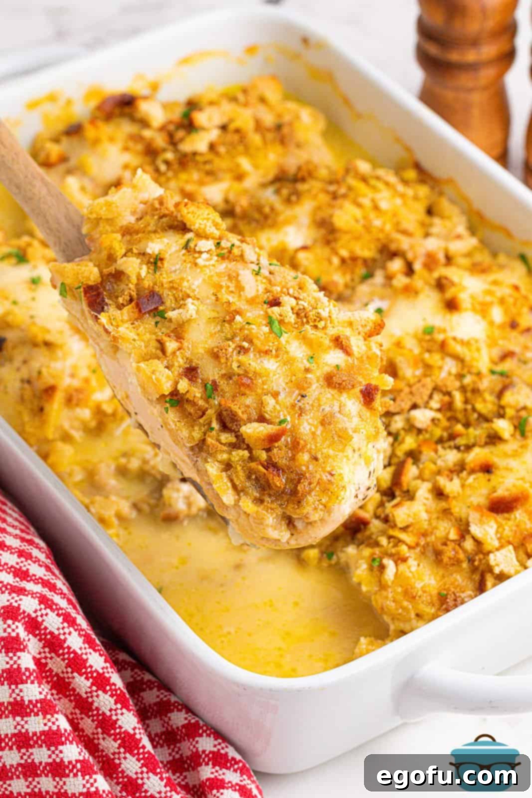 A wooden serving spoon holding a generous portion of creamy Swiss Chicken Casserole, showcasing the golden-brown stuffing topping and tender chicken.