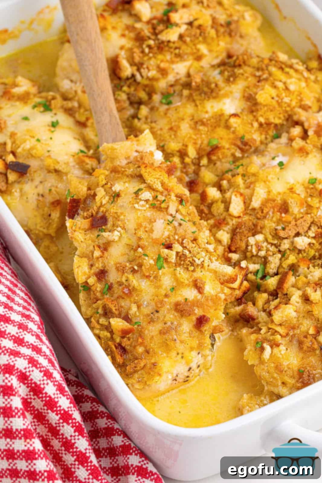 A wooden serving spoon scooping a portion of Swiss Chicken Casserole from the baking dish, showing the creamy chicken and crispy stuffing.