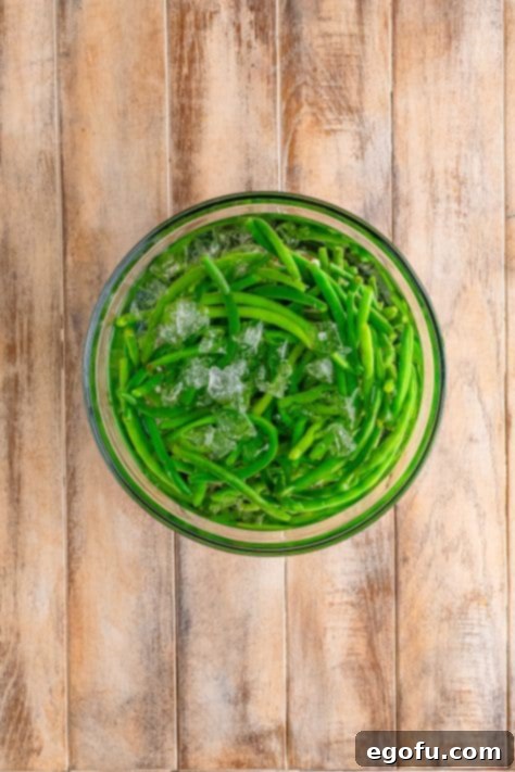 Cooked green beans in a bowl of ice cubes and water.