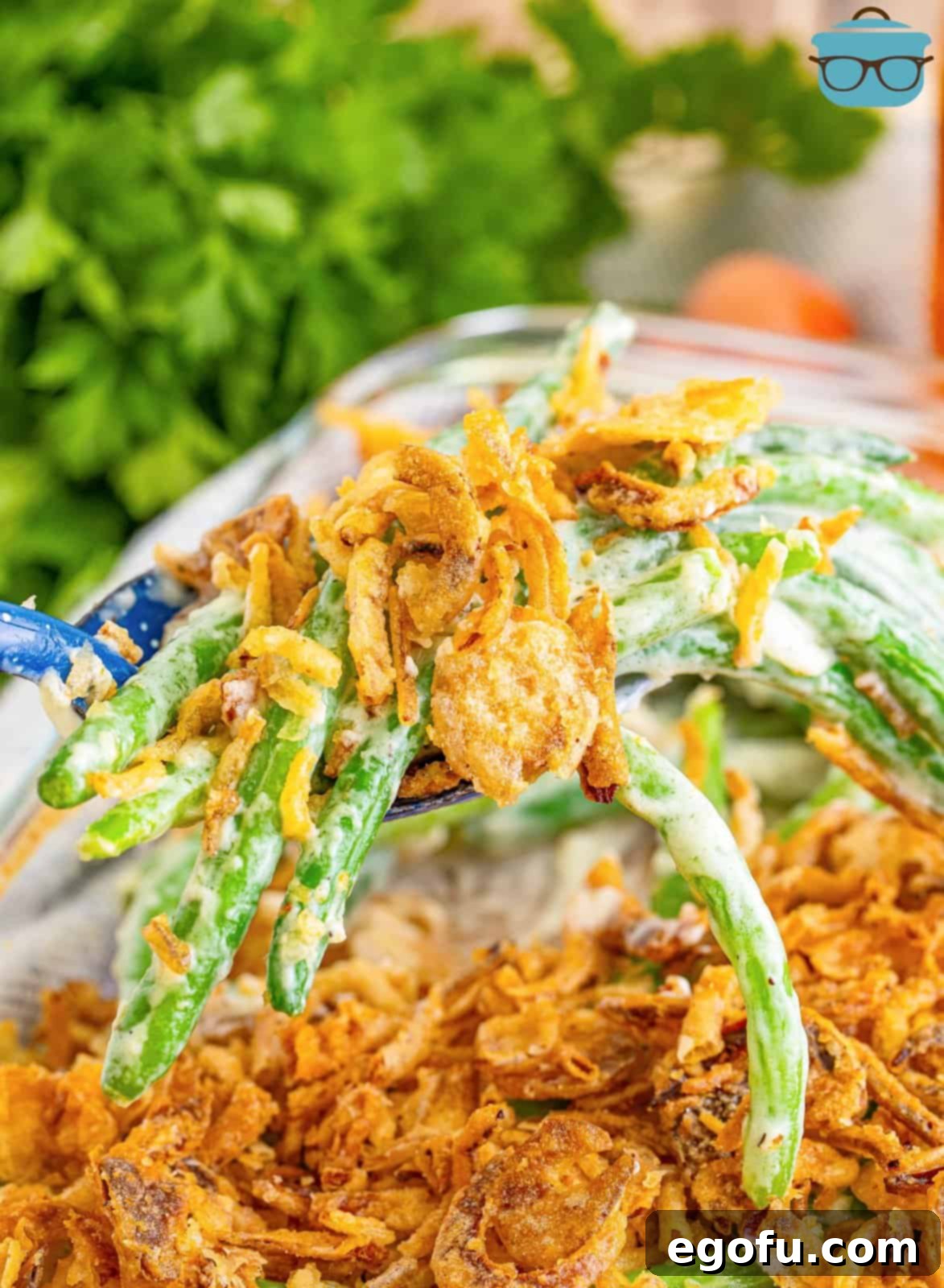 A scoop of Green Bean casserole with fried onions on top being held above the baking dish. 