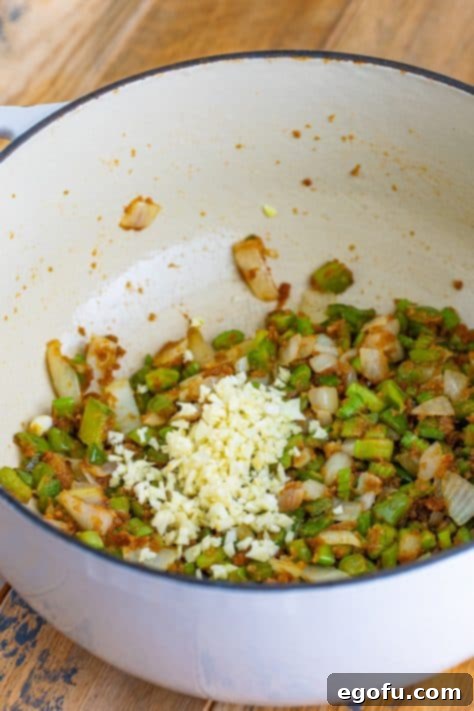 Minced garlic being added to the cooked vegetables and roux in a Dutch oven, releasing its fragrant aroma.