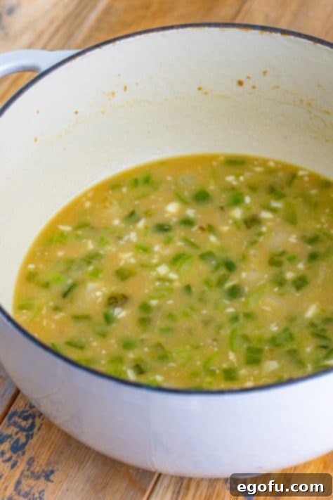 Chicken stock being slowly poured into the Dutch oven with the aromatic vegetables and roux, creating the rich base for the étouffée.