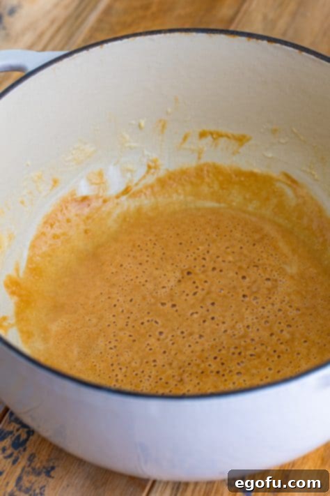 A smooth, peanut butter-colored roux, made from butter and flour, cooking in a Dutch oven.