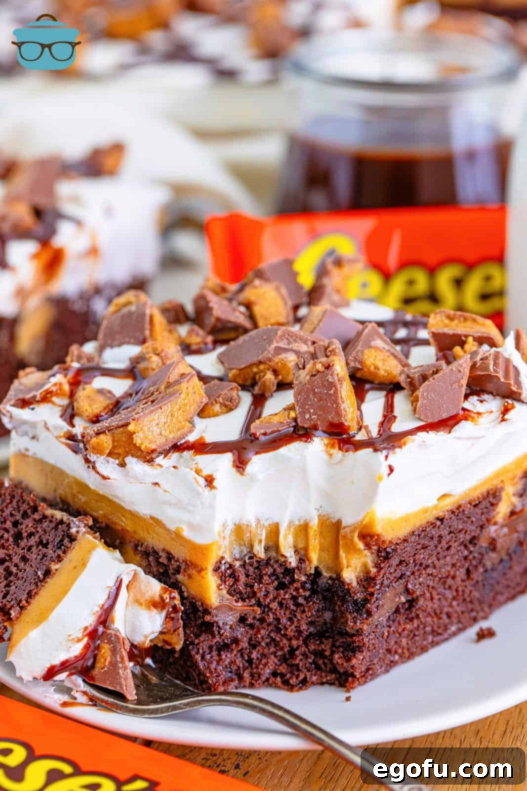 A fork holding a bite of Reese's Poke Cake next to a slice on a plate.