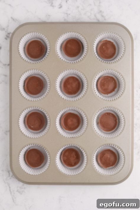 Reese's Peanut Butter Cheesecake Minis 10 A muffin tin, each well lined with cupcake wrappers and a Reese's cup in each one.