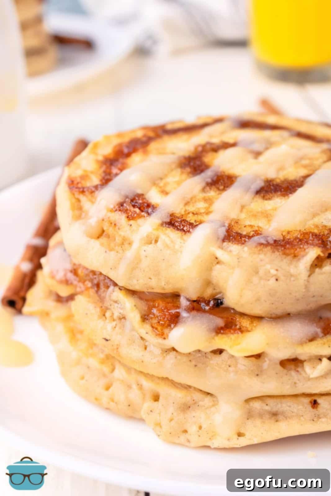 A close-up view of a beautifully glazed stack of Cinnamon Roll Pancakes, showing the distinct swirl.
