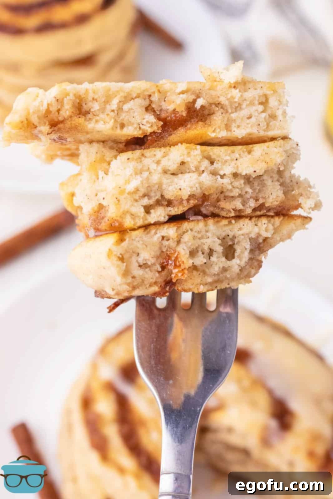 A fork taking a bite out of a Cinnamon Roll Pancake, revealing the fluffy interior and cinnamon swirl.